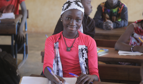 Young woman holds pen with paper in educational setting. Photo credit Right To Play