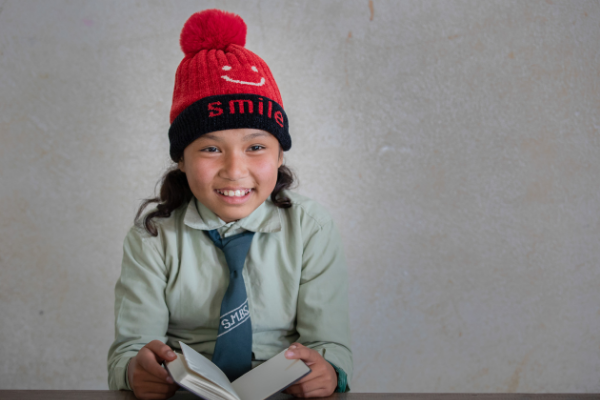 Smiling child reads book. Photo credit: Navesh Chitrakar/UWS