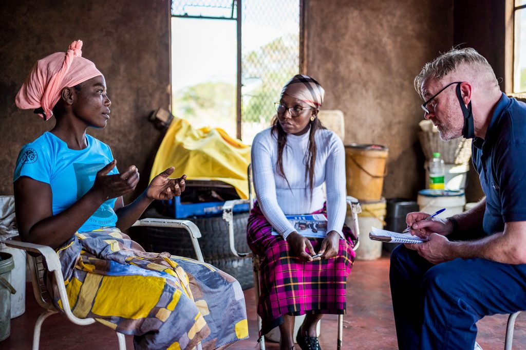 A young woman talks to a man with a notepad and pen while another woman listens in. Photo Trocaire