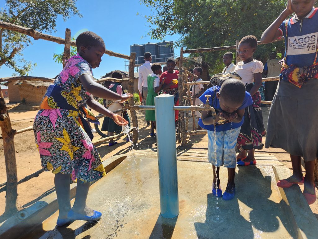 Two children drinking water from a water tap