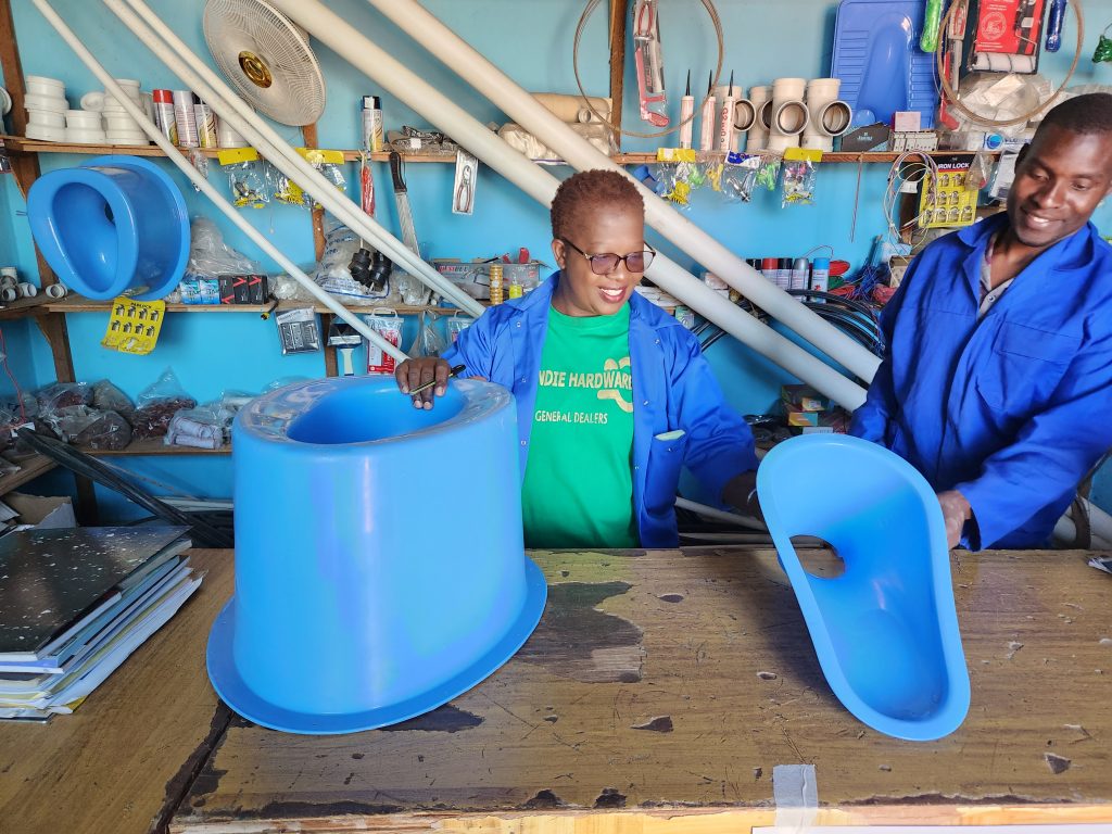 A woman and a man wearing blue uniform, stood in a sanitation shop and holding a portable toilet