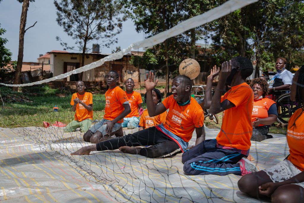 A group of children sat on the ground playing sports, laughing and smiling