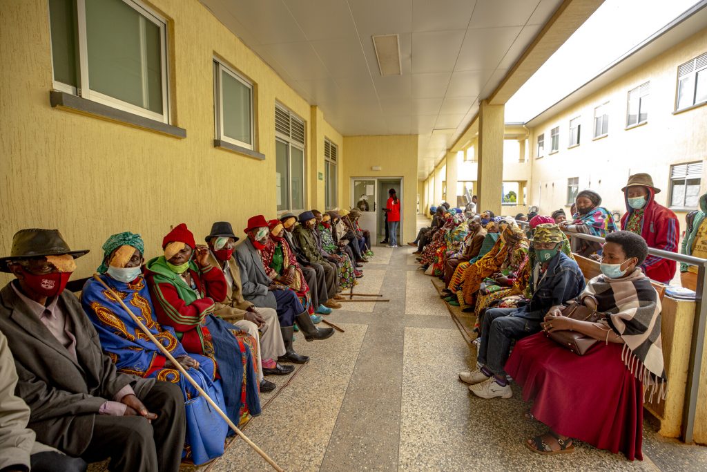 Around thirty people, all wearing eye patches after surgery, sitting along either side of a walkway. 