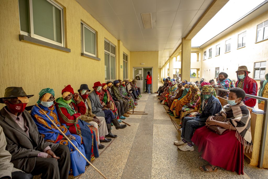 Around thirty people, all wearing eye patches after surgery, sitting along either side of a walkway.