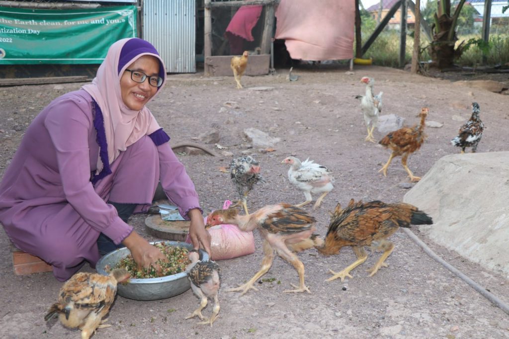 A woman knelt down feeding her chickens